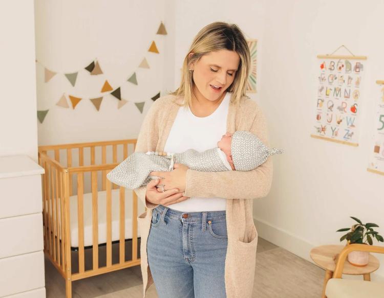 Mom cradling baby wrapped in a KeaBabies Soothe Swaddle Wrap wearing a matching knot hat.