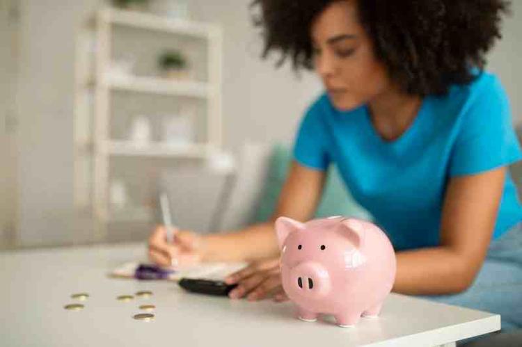 Serious concentrated millennial african american curly lady counting money near piggy bank in living