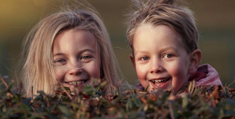  zwei Kinder mit blonden Haaren die lächelnd in die Kamera blicken