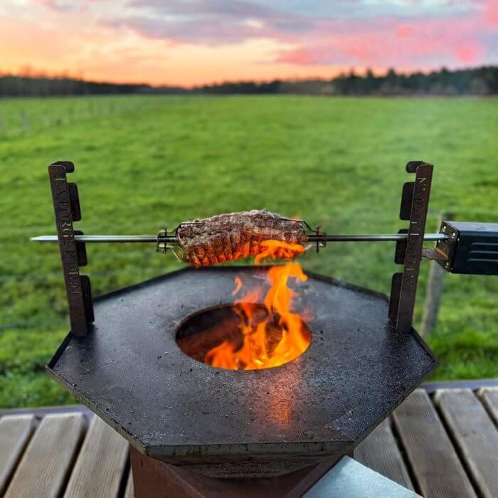 Rôti sur tourne-broche au-dessus du feu d'un brasero au coucher du soleil