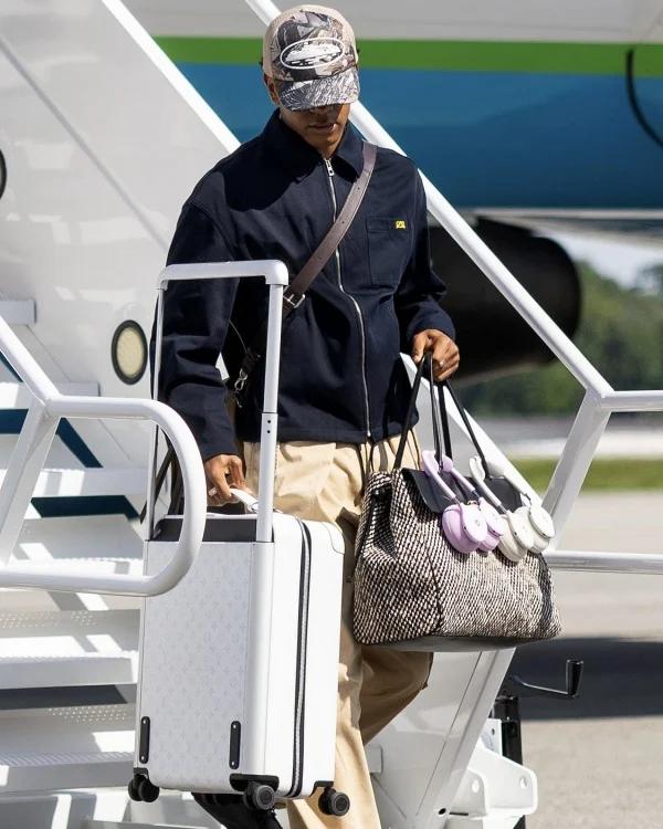 lamine yamal stepping off plane holding carry on bag with two pairs of beats headphones slung around the handles