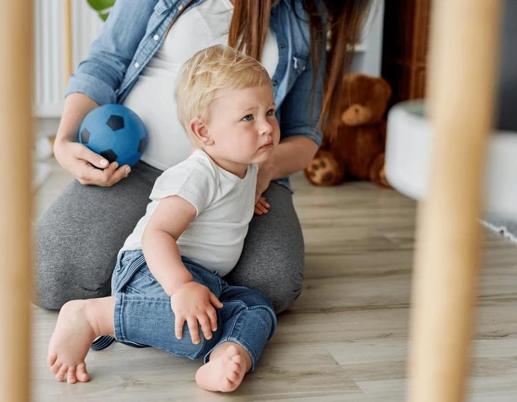Toddler throwing a tantrum on the living room floor while his mother sits calmly beside him.