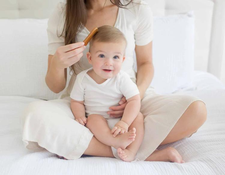 Mom gently combing baby's hair with infant brush and comb set.