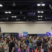A large crowd of people walk and gather at an indoor expo or convention, surrounded by vendor booths and colorful banners under bright overhead lights—an exciting opportunity to become a sponsor and boost your brand’s visibility. Austin Marathon Half Marathon & 5K