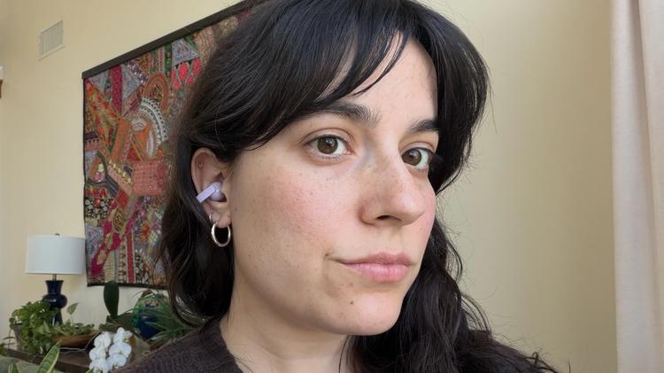 woman standing in front of tapestry wearing purple clip on earbuds