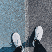 A person wearing white sneakers stands with one foot on a blue surface and the other on gray pavement, separated by a white line—reflecting on how to handle a missed long run and seeking running tips for next time. Austin Marathon Half Marathon & 5K