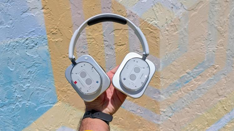 man's hand holding up a pair of Nothing headphones against mural