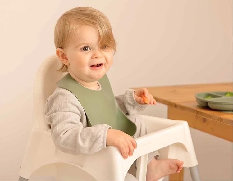 Baby self-feeding sliced vegetables in a high chair.