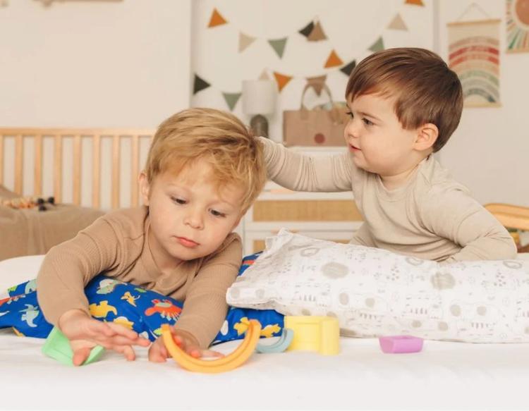 Toddlers playing on a bed with eco-friendly toys and a soft, child-safe pillow, creating a cozy and sustainable playtime environment indoors.