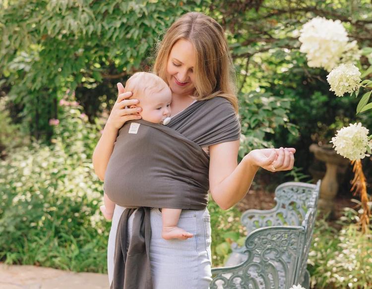 Mother babywearing with an ergonomic KeaBabies D-Lite Wrap Carrier during a walk in the park.