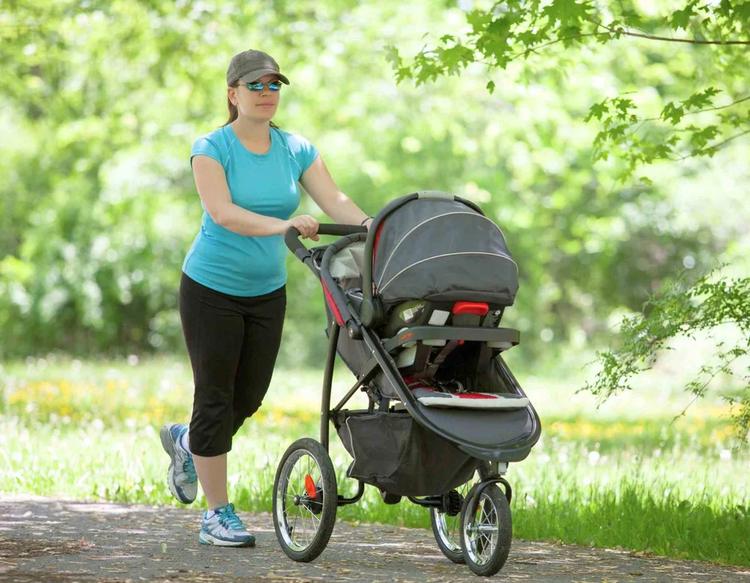 Young woman pushing a stroller on a hot summer day while keeping her baby shaded and comfortable outdoors.