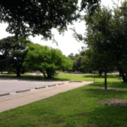 A mostly empty parking lot next to a grassy area with trees, under a clear sky—a peaceful spot often passed by those exploring Running routes Austin. Curb stops are visible, and sunlight filters through the branches. Austin Marathon Half Marathon & 5K