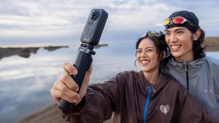Two people looking at a Insta360 X6 camera on a selfie stick.