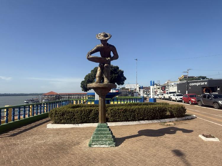 Foto colorida de monumento de homenagem aos garimpeiros em Itaituba (PA). Ao fundo, casas e rio
