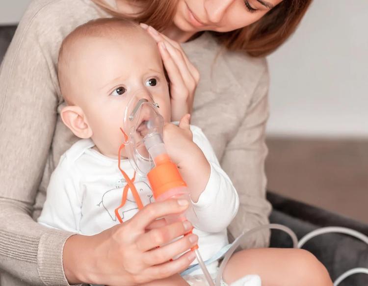 Mother using nebulizer for cute little baby at home.