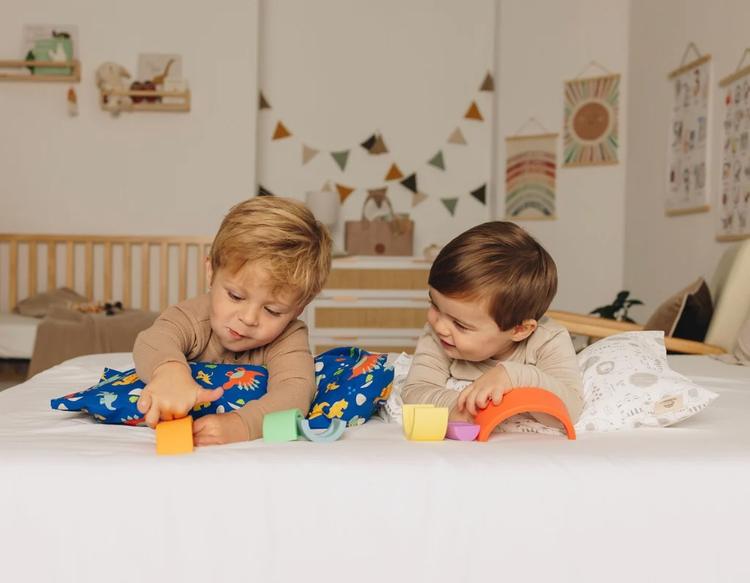 Two toddlers sitting in bed together, playing with toys.