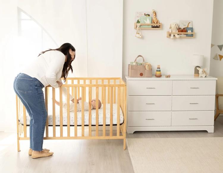 Mom checking on baby lying on a crib sheet in a well-designed, organized nursery room with a calm and tidy setup.