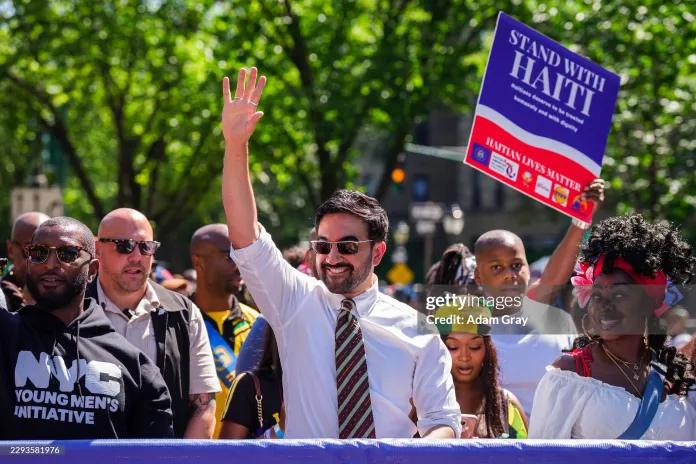 New York City Mayor Zohran Mamdani marches in the annual West Indian American Day Carnival Parade on September 7, 2026 in the Brooklyn borough of New York City as a parade goer holds a sign on TPS. 