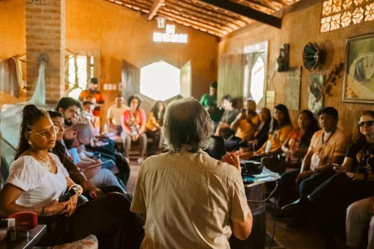 Foto colorida de Lula do Mel, de costas, falando com grupo de visitantes em sala do Solar das Abelhas, em Caruaru