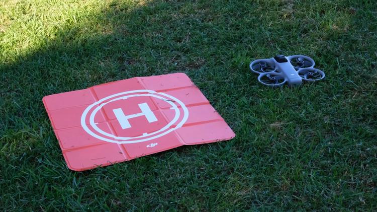 The DJI Avata 360 in the grass next to its bright orange landing pad.