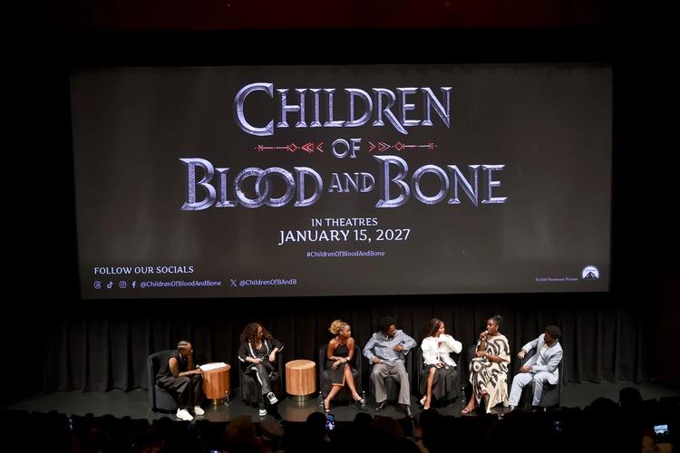 A group of people sitting on stage in front of a large movie poster for 